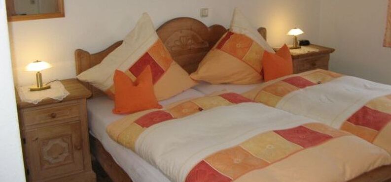 Bett mit oranger Bettwäsche. 