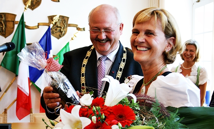 Bürgermeister Hofauer und eine Damen mit Blumen in der Hand lachen in die Kamera.