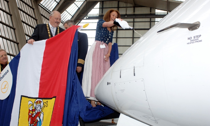 Der Bürgermeister hält die Fahne mit dem Stadtwappen Altöttings, währen ein Flugzeut getauft wird. 