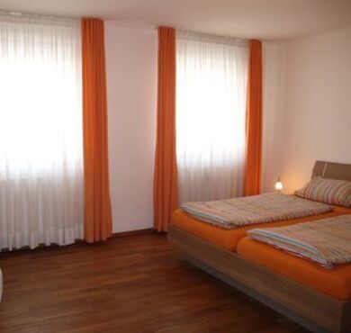 Schlafzimmer mit Bett und orangen Vorhängen. 