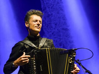 Ein Mann mit Akkordeon vor einem blauen Hintergrund.