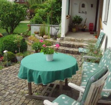 Ein runder Gartentisch auf einer Terrasse mit Bank und Stühlen. 