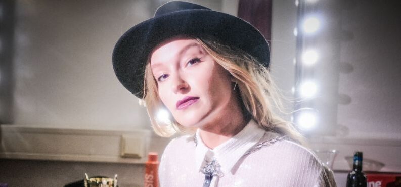 Die junge Kabarettistin Malarina posiert mit Hut vor einem Garderobenspiegel.