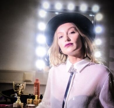 Die junge Kabarettistin Malarina posiert mit Hut vor einem Garderobenspiegel.