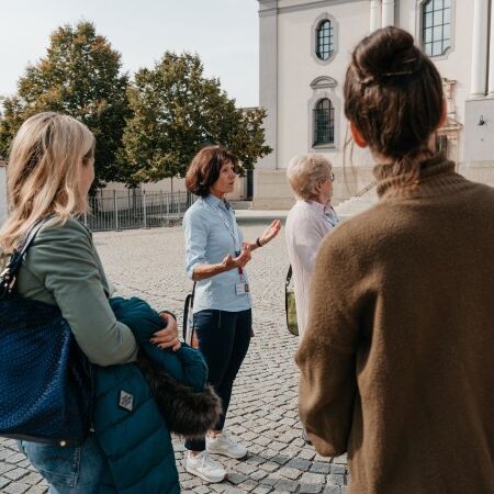 Eine Stadtführerin steht vor der Basilika und erklärt ihrer Gruppe etwas.