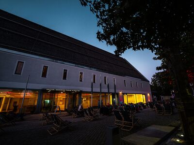 Kino, Picknick, Altötting, Zuccalliplatz, Sommer, Bild Lukas Fischer Menschen sitzen auf Liegestühlen am Abend vor einem Gebäude.