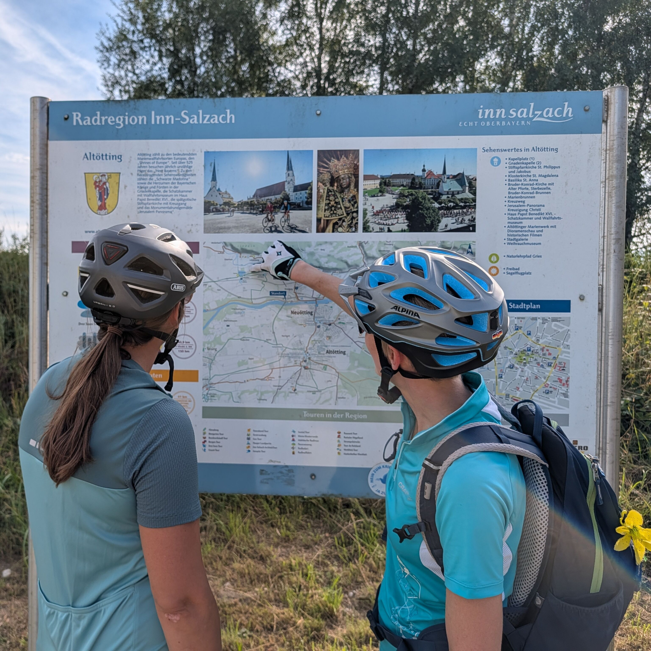 Zwei Radlfahrerinnen betrachten eine Übersichtstafel von Radwegen um Altötting.