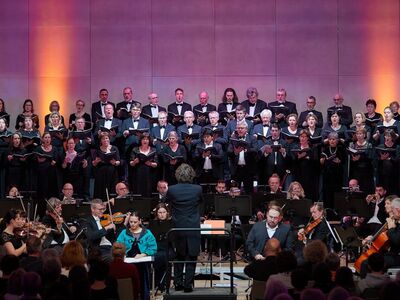 Musiker und Orchester stehen vor einer rot beleuchteten Wand.