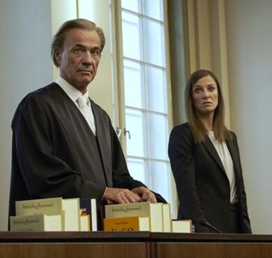 Eine Mann und eine Frau in Rechtsanwaltsrobe im Gerichtssaal.