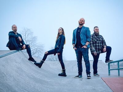 Drei Männer und eine Frau in dunkler Bekleidung stehen nebeneinander.