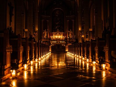 Ein Mittelgang in der einer Kirche nur mit Kerzen beleuchtet.
