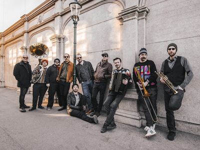 Gewürztraminer, Da gemischte Satz, Balkan-Gypsy-Swing, Forum Altötting, Bild Veranstalter Zehn Musiker lehnen an einer Wand und haben Instrumente in der Hand.