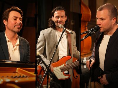 Drei Musiker mit Klavier, Gitarre und am Schlagzeug.