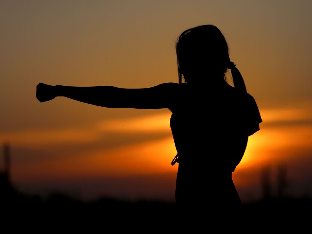 Silhouette einer Frau während des Kampfsporttrainings vor Sonnenuntergang