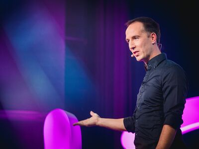 Die Kunst zu Leben, Steffen Kirchner, Forum, Altötting, Bild Veranstalter Ein Mann in dunklem Hemd vor einem bunten Hintergrund.