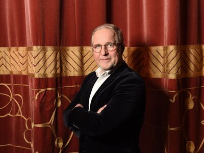Der Schauspieler Harald Krassnitzer steht vor einem roten Samtvorhang.