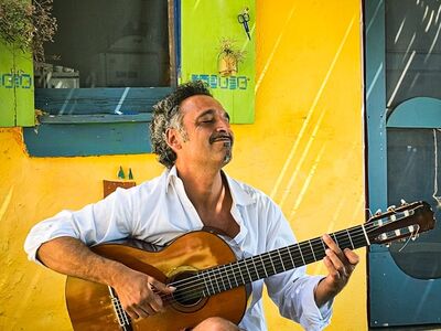 Ein Mann sitzt mit einer Gitarre vor eine bunten Hauswand.