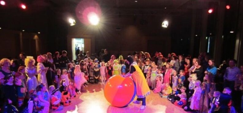 Kinderfasching, Kultur+Kongress Forum Altoetting, Foto Shilly Shally Company Eine Gruppe von Kindern stehen verkleidet um einen Clown.