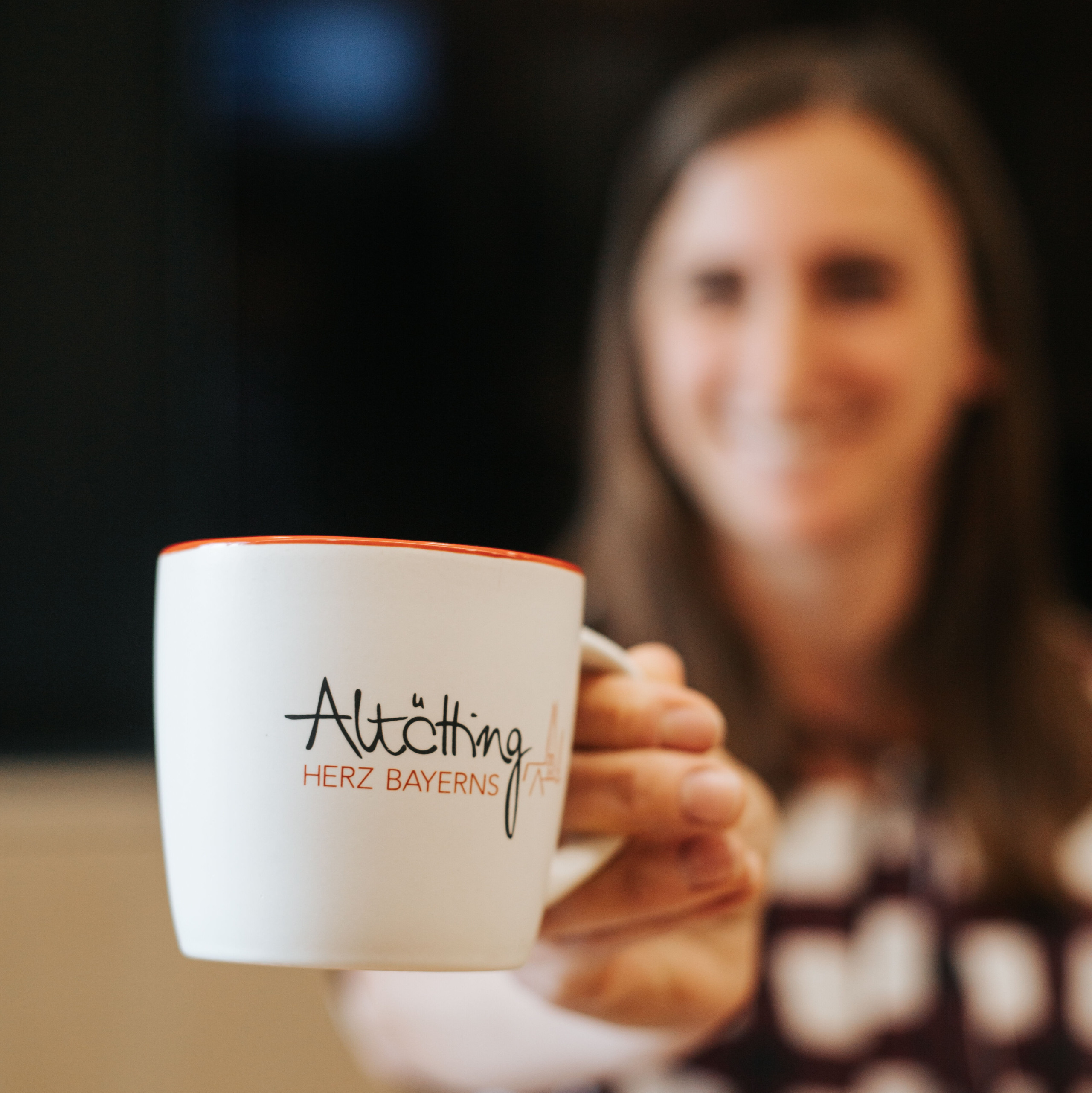 Eine Frau hält eine Tasse mit Aufschrift Altötting Herz Bayerns in die Kamera. 