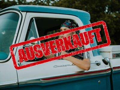 Eine junge Frau mit Kopftuch sitzt in einem alten Auto.