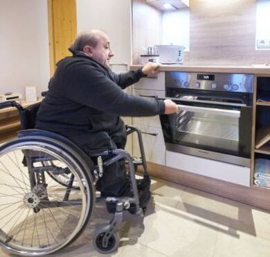 Ein Rollstuhlfahrer öffnet den Ofen in der Küche.