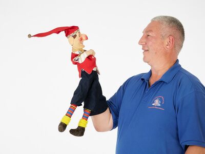 Ein Mann hält eine Handpuppe in die Höhe.