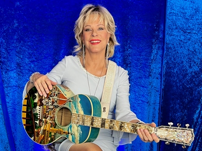Lisa Fitzt sitzt mit ihrer Gitarre vor einem blauen Hintergrund.