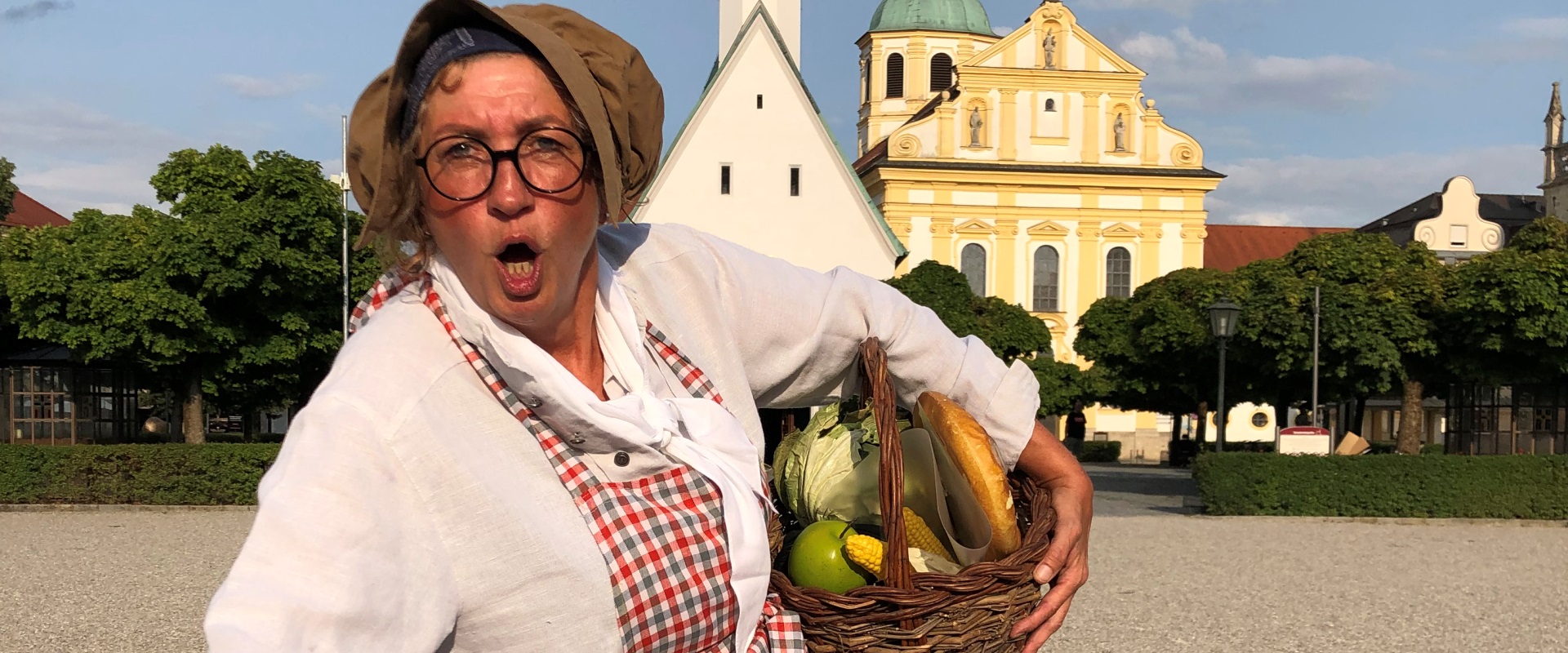 Eine alte Marktfrau steht mit einem Obstkorb am Kapellplatz.