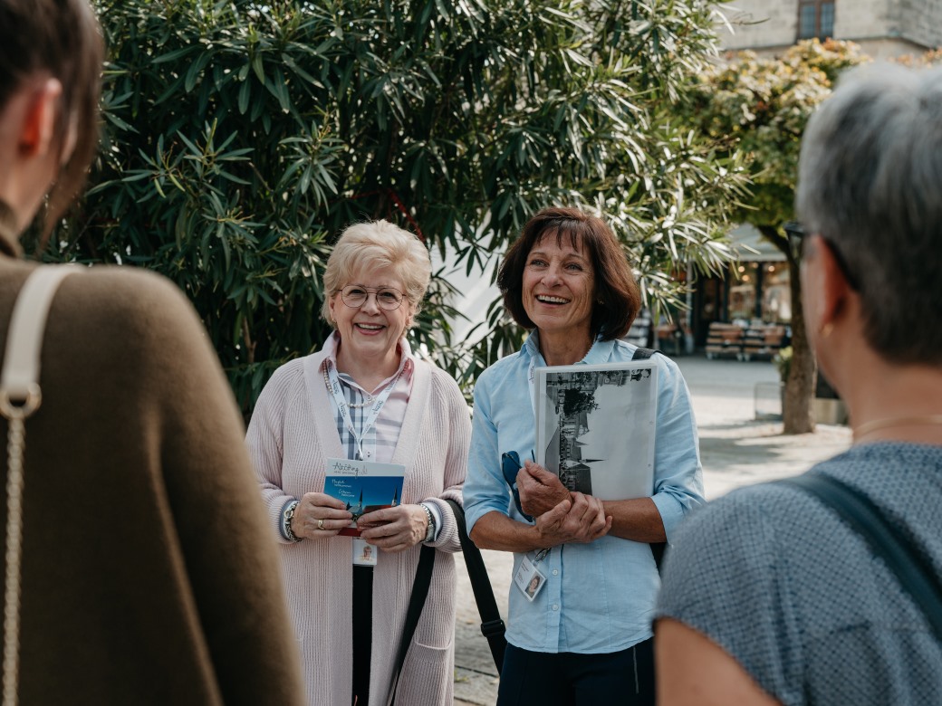 Zwei Stadtführerinnen stehend lachend vor ihrer Frauengruppe. 