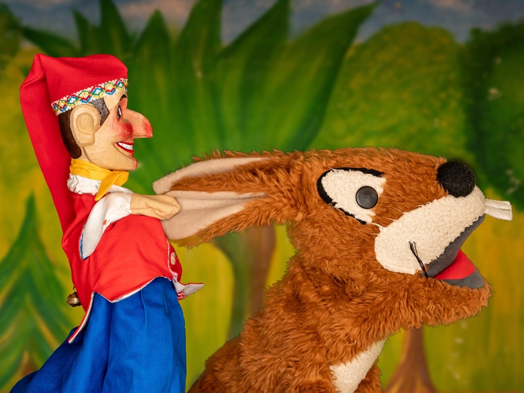 Holzpuppe Kasperl und ein Stoffhase auf der Puppenbühne.