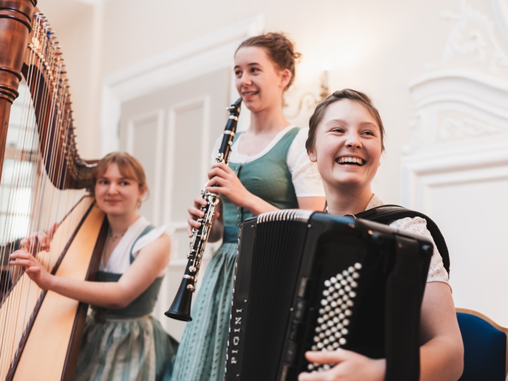 Drei junge Frauen musizieren mit Harfe, Klarinette und Ziehharmonika.