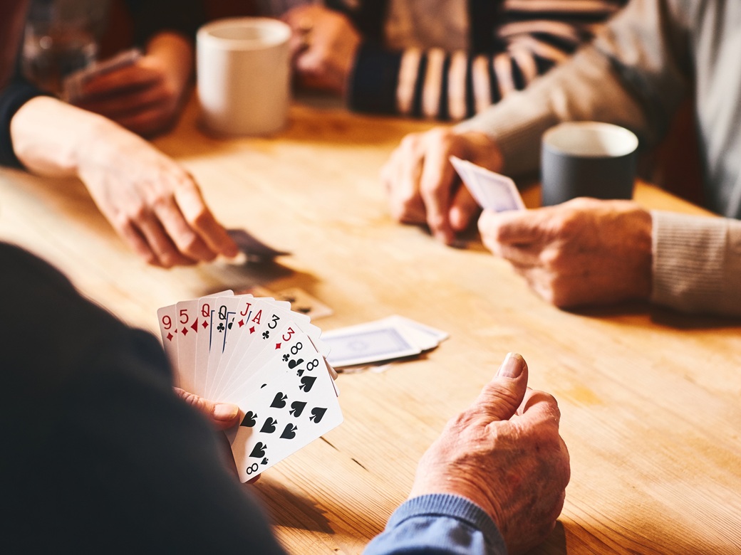 Senioren sitzen an einem Tisch und spielen ein Kartenspiel