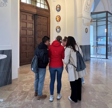 Vier Personen stehen in der Basilika vor den Papstwappen.