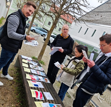 Vier Personen stehen vor einer Bank und lösen ein Bildersortierrätsel.