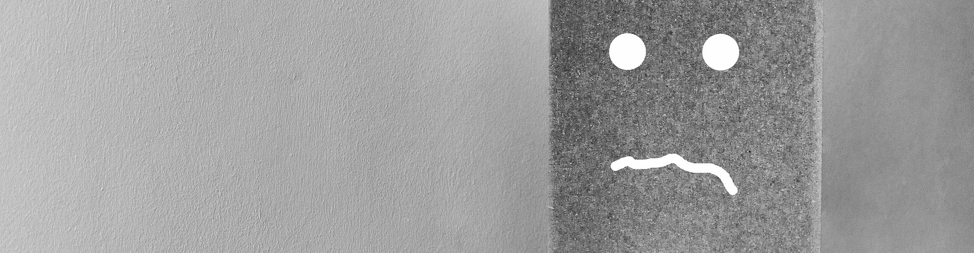 Auf einer grauen Wand ist ein trauriger Smiley gemalen. 