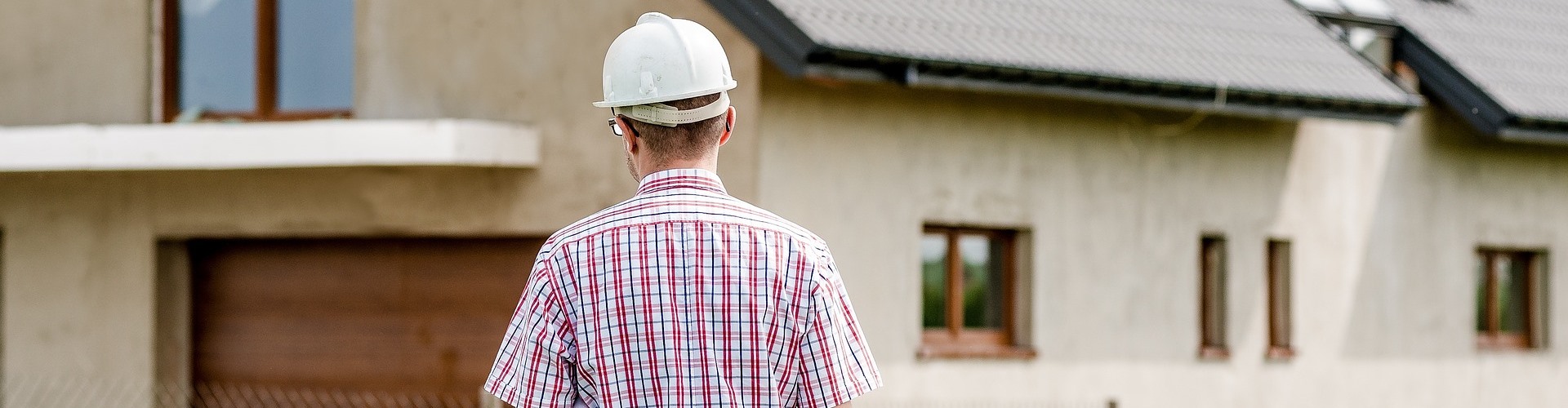 Ein Herr mit Helm begutachtet ein Haus.