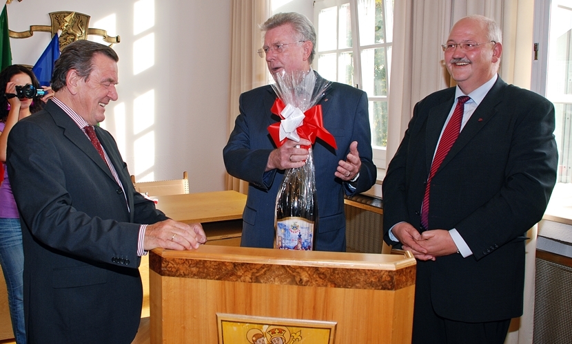 Der Bundeskanzler a. D. Gerhard Schröder bekommt bei seinem Besuch in Altötting 2009 von dem damaligen Bürgermeister von Mühldorf Günther Knoblauch eine große Bierflasche geschenkt.