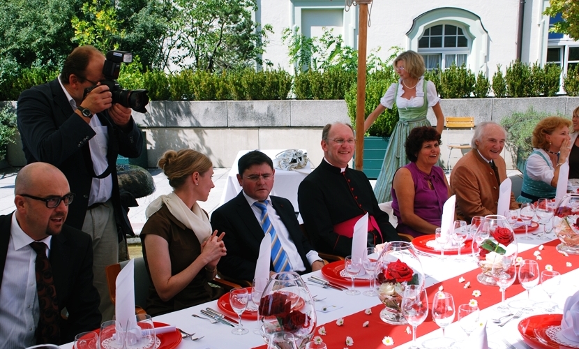 Ehrengäste sitzen am in rot gedeckten Tisch.