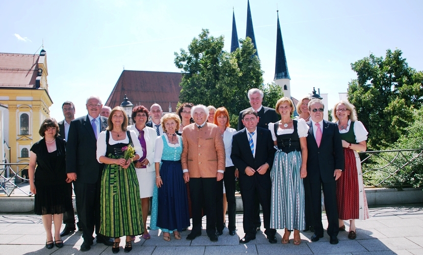 Gruppenbild der Ehrengäste auf der Terrasse Hotel Zur Post mit der Stiftspfarrkirche im Hintergrund.