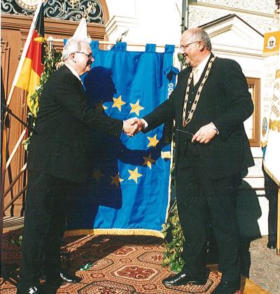 Bürgermeister Hofauer schüttelt einem Ehrengast vor der Europafahne die Hand. 