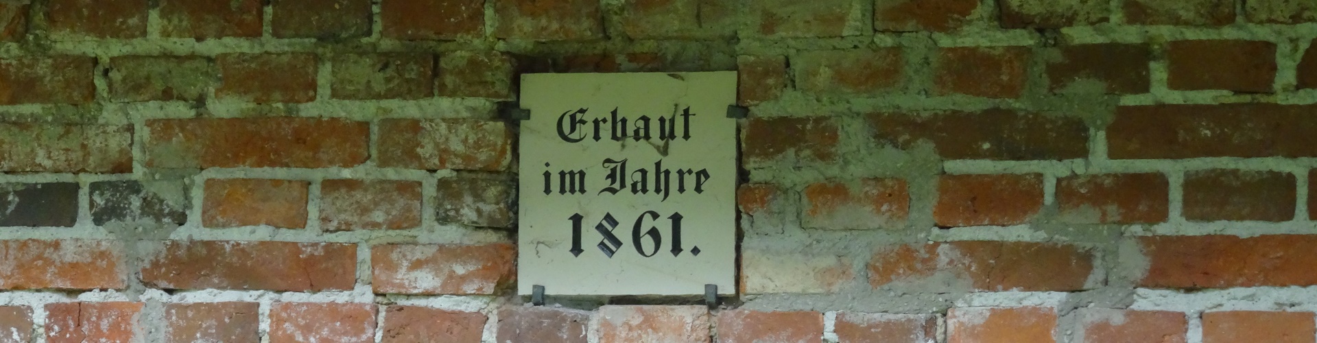 Das Erbauungsschild des Freibad Altötting hängt an einer Backsteinmauer.