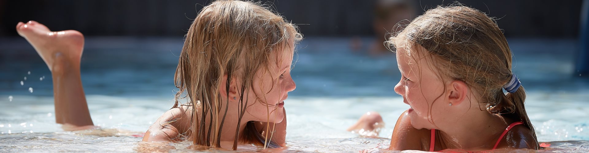 Zwei Mädchen liegen im Freibad im Kinderbecken im Wasser.