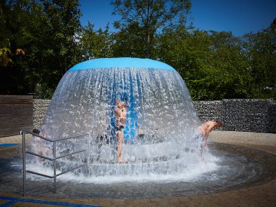 Zwei Männer lassen sich im Freibad St. Georgen vom Wasserfall des Massagepilzes den Rücken massieren.