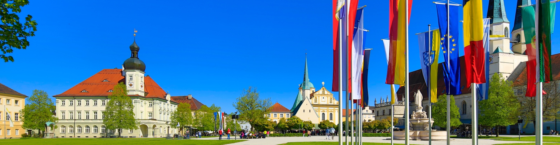 Außenansicht auf das Altöttinger Rathaus mit Fahnen im Vordergrund.