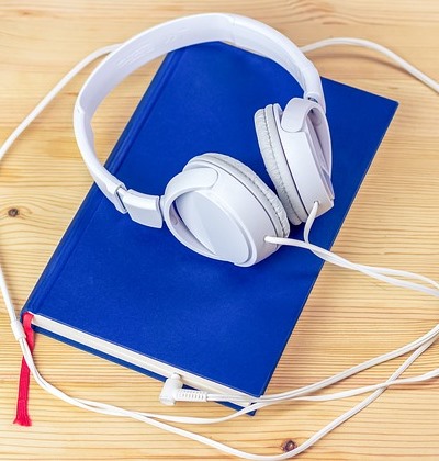 Kopfhörer liegen auf einem blauen Buch, die Kabel sind in das Buch gesteckt.