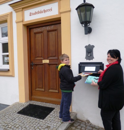 Mutter und Sohn geben bei der Stadtbücherei über die Medienbox neben der Eingangstür zur Bücherei Bücher zurück.