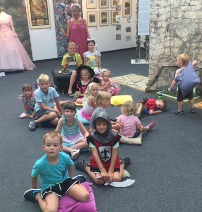 Büchereileiterin Sonja Zwickl mit vielen Kinder, die am Boden sitzend zuhören, bei der Vorlese3viertelstunde zum Thema Märchenhaft in der Stadtgalerie Altötting.