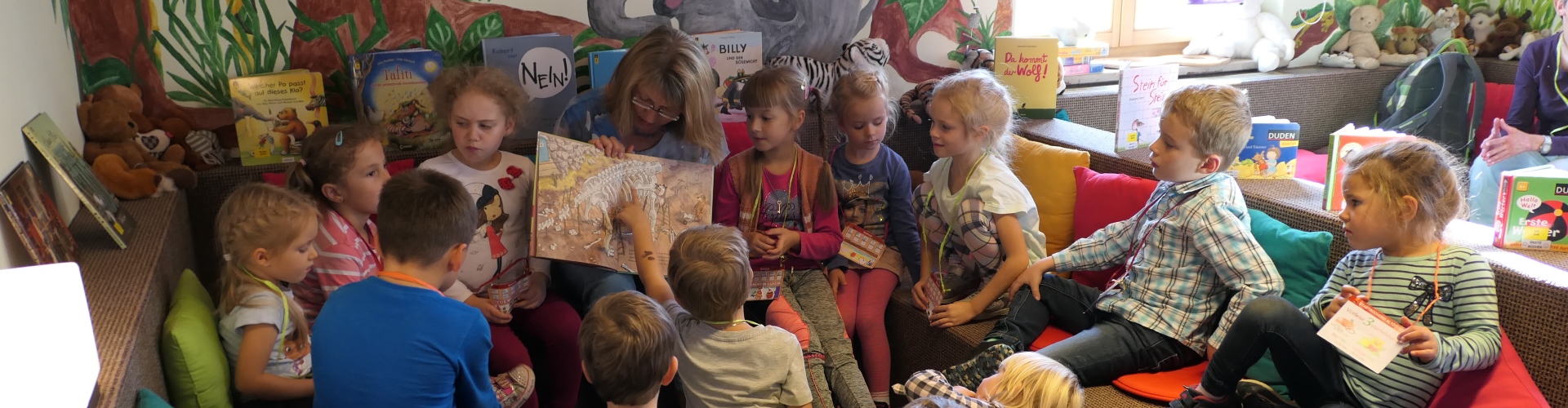 Kinder hören bei der Vorlese3viertelstunde in der Stadtbücherei Altötting aufmerksam der Vorleserin zu.