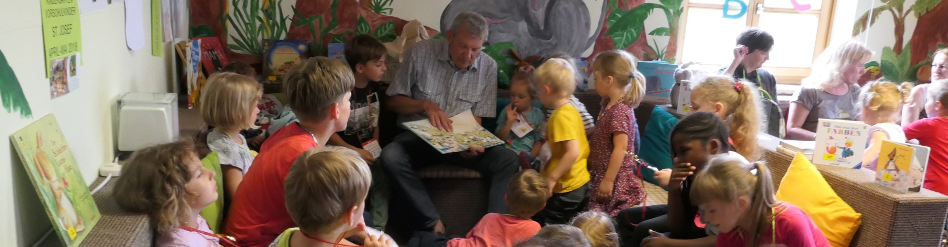 Kinder hören bei der Vorlese3viertelstunde in der Stadtbücherei Altötting aufmerksam dem vorlesenden Werner Sirringhaus zu.