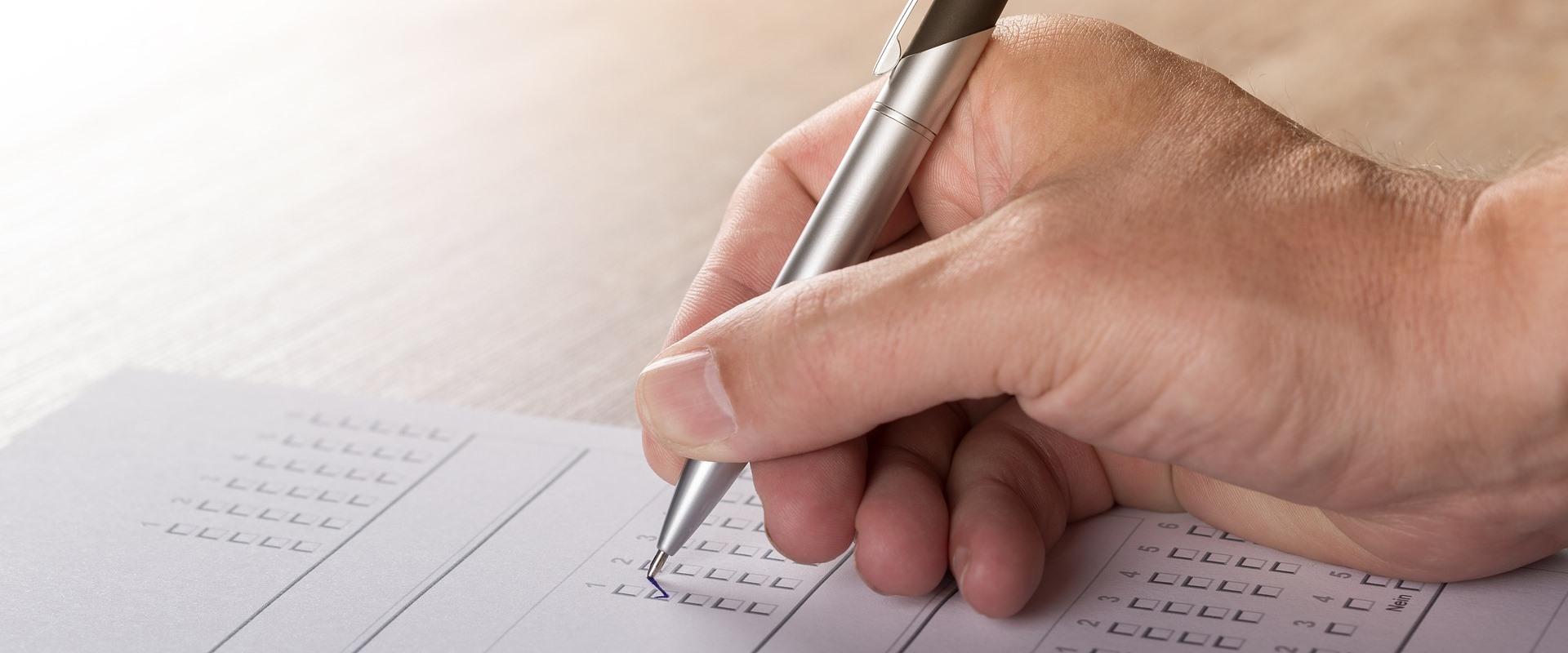 Nahaufnahme einer Hand mit Stift, die gerade einen Wahlstimmzettel ausfüllt.